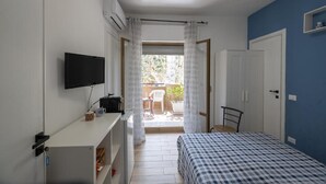 Ein Schlafzimmer mit Bett, Fernseher, Schreibtisch und einem Balkon mit Sitzgelegenheit.