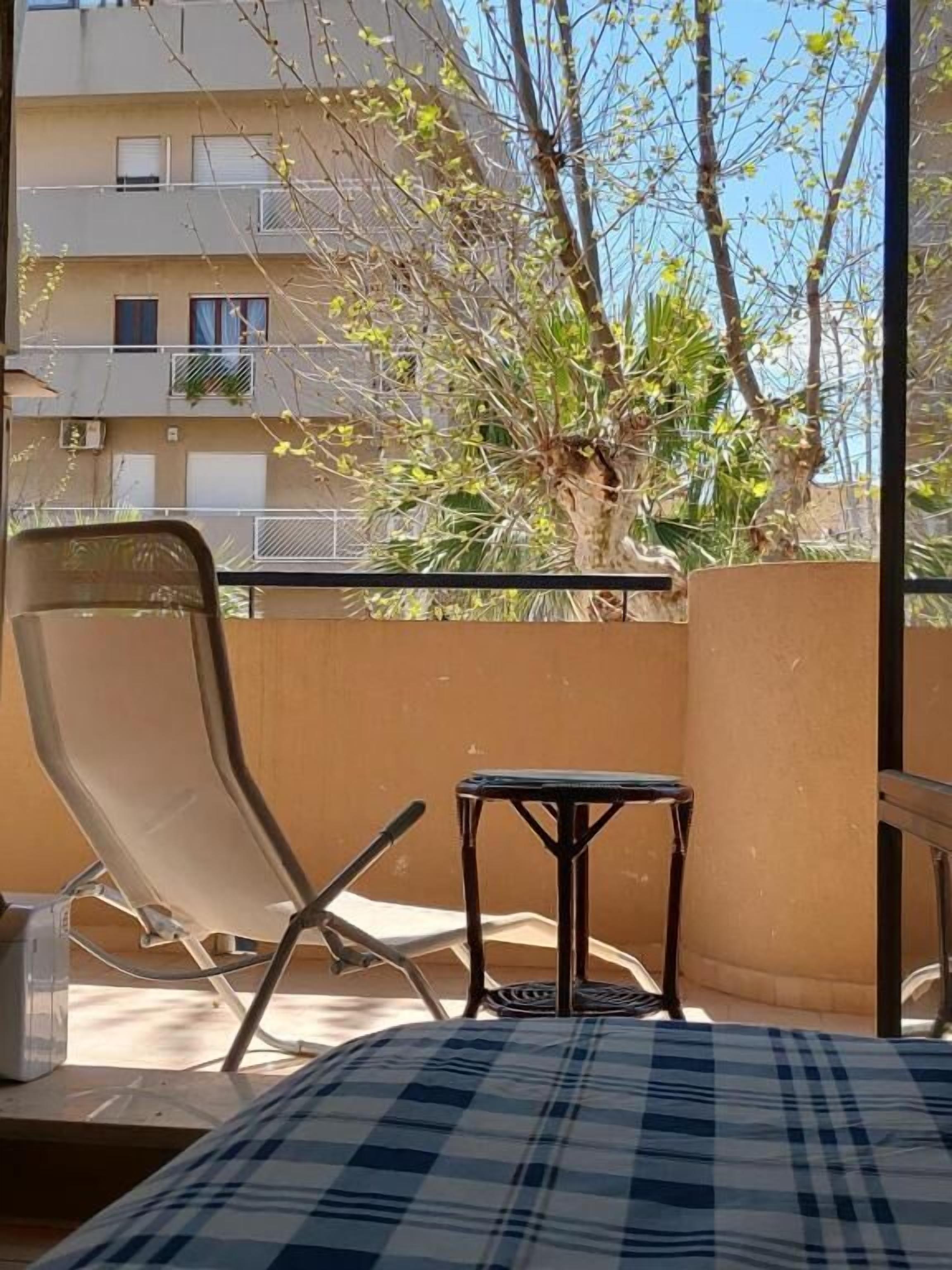Un balcone con una sedia, un tavolino e vista su un edificio e degli alberi.