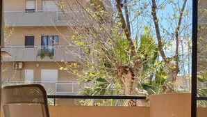 Ein Balkon mit Stuhl, Tisch und Blick auf ein Gebäude und Bäume.