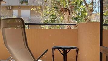 Un balcone con una sedia, un tavolino e vista su un edificio e degli alberi.