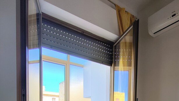 Ein modernes Zimmer mit einer Schiebetür zu einem Balkon, einem schwarzen Stuhl und einem weißen Wäscheständer.
