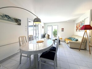 Ein Essbereich mit einem runden Tisch, Stühlen und einer Lampe. Außerdem ein Sofa und ein Bild an der Wand.