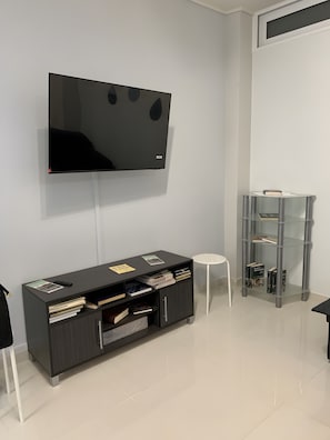 Ein modernes Wohnzimmer mit einem an der Wand befestigten Flachbildfernseher, einer dunkelholzmöbel-Unterhaltungsecke mit Büchern und einem kleinen Tisch sowie einer Glastrennwand mit Büchern.