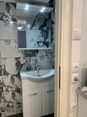 Ein Badezimmer mit einem weißen Waschbecken, einem Spiegel darüber und Wänden mit Marmoroptik.