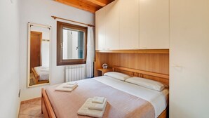 A bedroom with a wooden ceiling, a bed with white bedding, a nightstand, a mirror, and a window with a curtain. - Apartment 'La Casa Di Giorgia' with Wi-Fi and Air Conditioning (Chioggia)