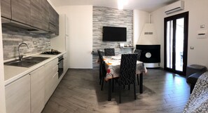 Eine moderne Küche mit eingebautem Herd, einem Essbereich mit Tisch und Stühlen, einem an der Wand montierten Flachbildfernseher und einem Kamin.
