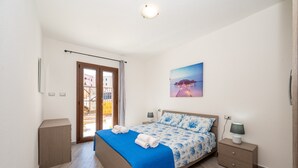 Une chambre à coucher comprenant un lit, une table de chevet, une lampe, un tableau accroché au mur et une porte donnant sur un espace extérieur.