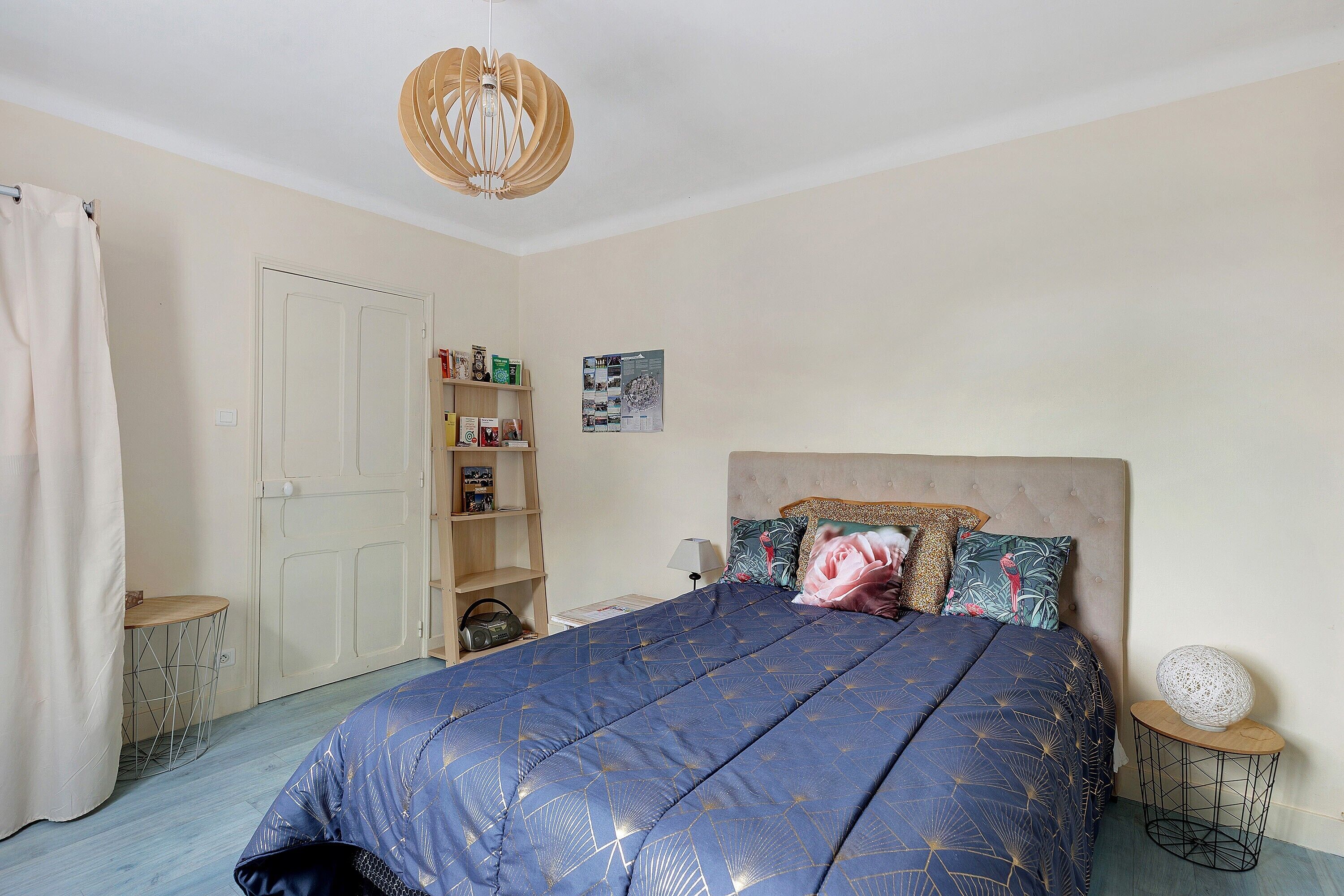 A bedroom with a bed, a bedside table, a lamp, a shelf with books, and a door.