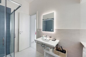 Une salle de bain moderne avec une douche à parois de verre, un lavabo blanc avec un miroir au-dessus et un porte-serviettes.