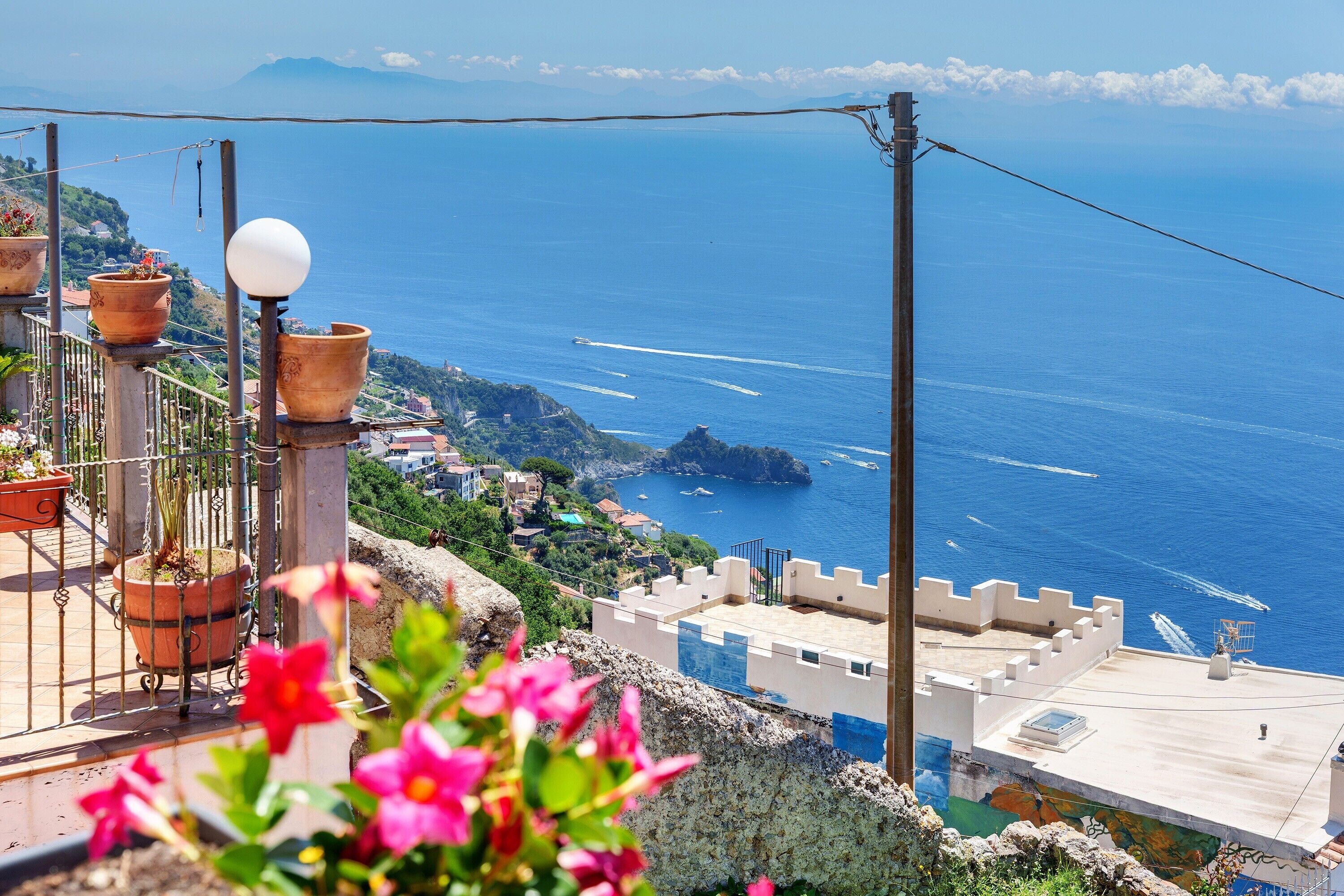 A coastal view with terraced buildings, potted plants, and a clear blue sea.