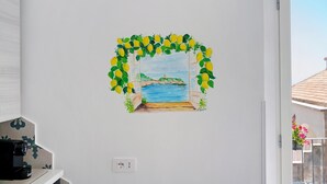 Un mur orné d’une peinture représentant une fenêtre donnant sur une plage, une porte blanche et une prise de courant.