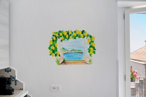 Un mur orné d’une peinture représentant une fenêtre donnant sur une plage, une porte blanche et une prise de courant.