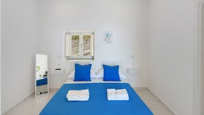 Une chambre à coucher avec un lit, deux oreillers, un miroir, une fenêtre et une œuvre d’art accrochée au mur.