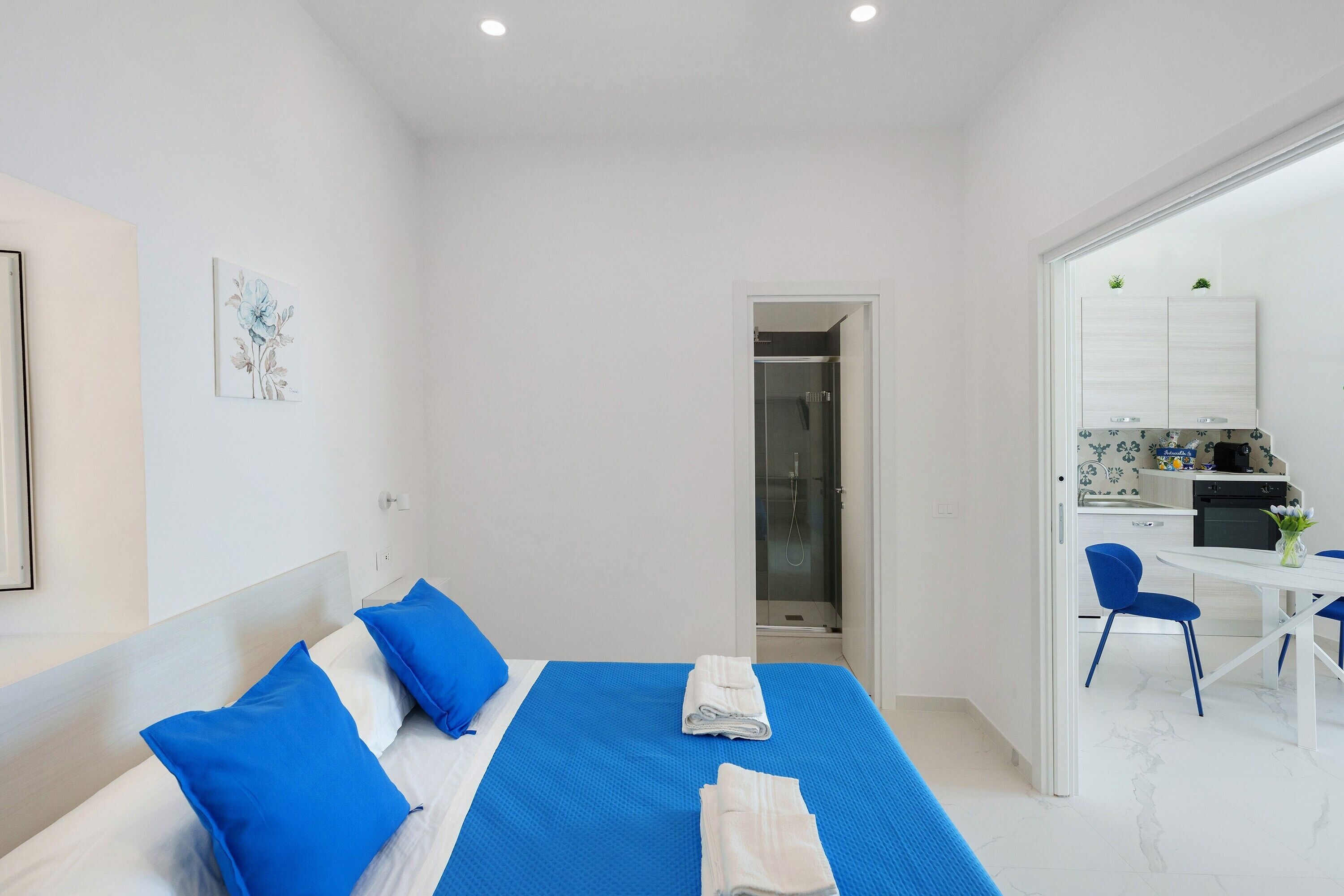 Habitación de hotel con cama, una pequeña kitchenette y un baño visible a través de una puerta abierta.