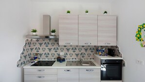 Une cuisine compacte équipée d’un évier, d’une cuisinière et d’un four, avec des meubles de couleur bois clair et un pare-feu décoratif.