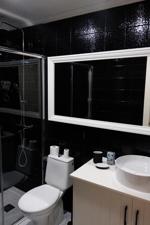 Un bagno con cabina doccia in vetro, un water, un lavandino e uno specchio.