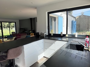 Een moderne keuken met een groot eiland, een zithoek met een bank en stoelen, en uitzicht door grote ramen.