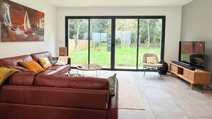 Ein Wohnzimmer mit braunem Ledersofa, einem Couchtisch, einem Fernseher auf einem Holzboden und einem Bild von Segelbooten.