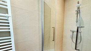 Ein modernes Badezimmer mit einer gläsernen Duschkabine, einem weißen Fliesenboden und einem an der Wand befestigten WC.