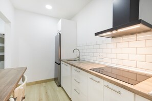 Eine kompakte Küche mit weißen Schränken, einer Holz Arbeitsplatte, einem Edelstahl-Kühlschrank und einer schwarzen Dunstabzugshaube.