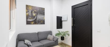 Uma sala de estar moderna com um sofá cinzento, uma mesa de centro de madeira, uma pintura de Buda, uma planta em vaso e uma porta preta.