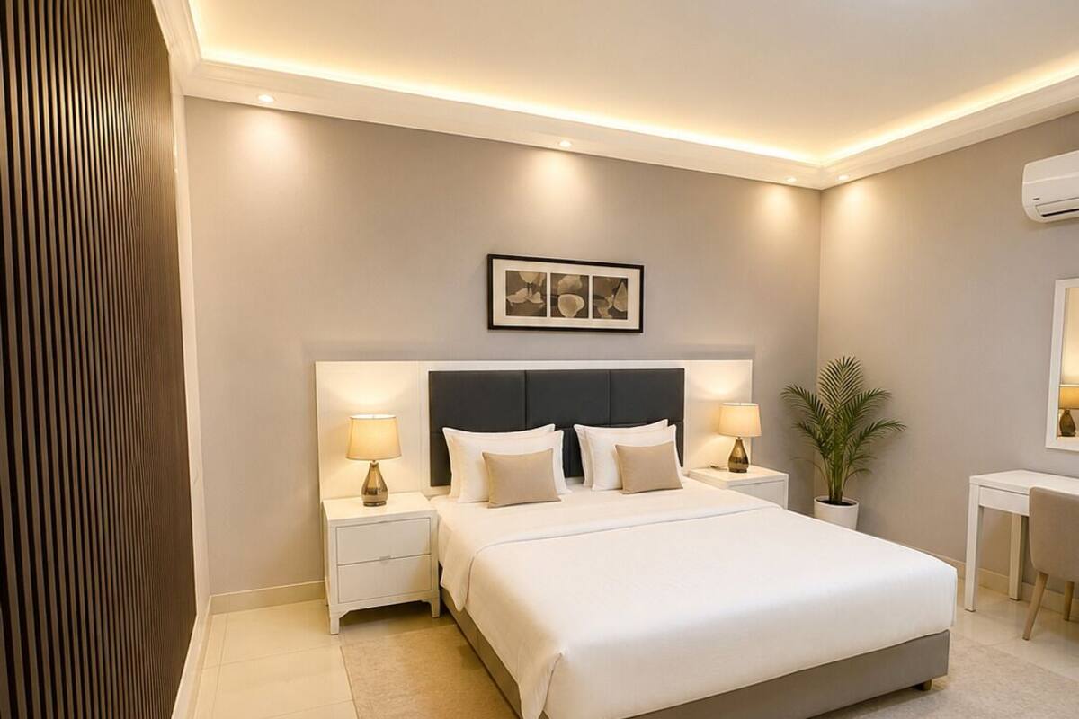 A modern bedroom with a large bed, bedside tables with lamps, a small desk, and a potted plant.