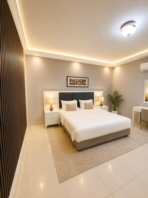 A modern bedroom with a large bed, bedside tables with lamps, a small desk, and a potted plant. - Open Hospitality Hotel (Dammam)