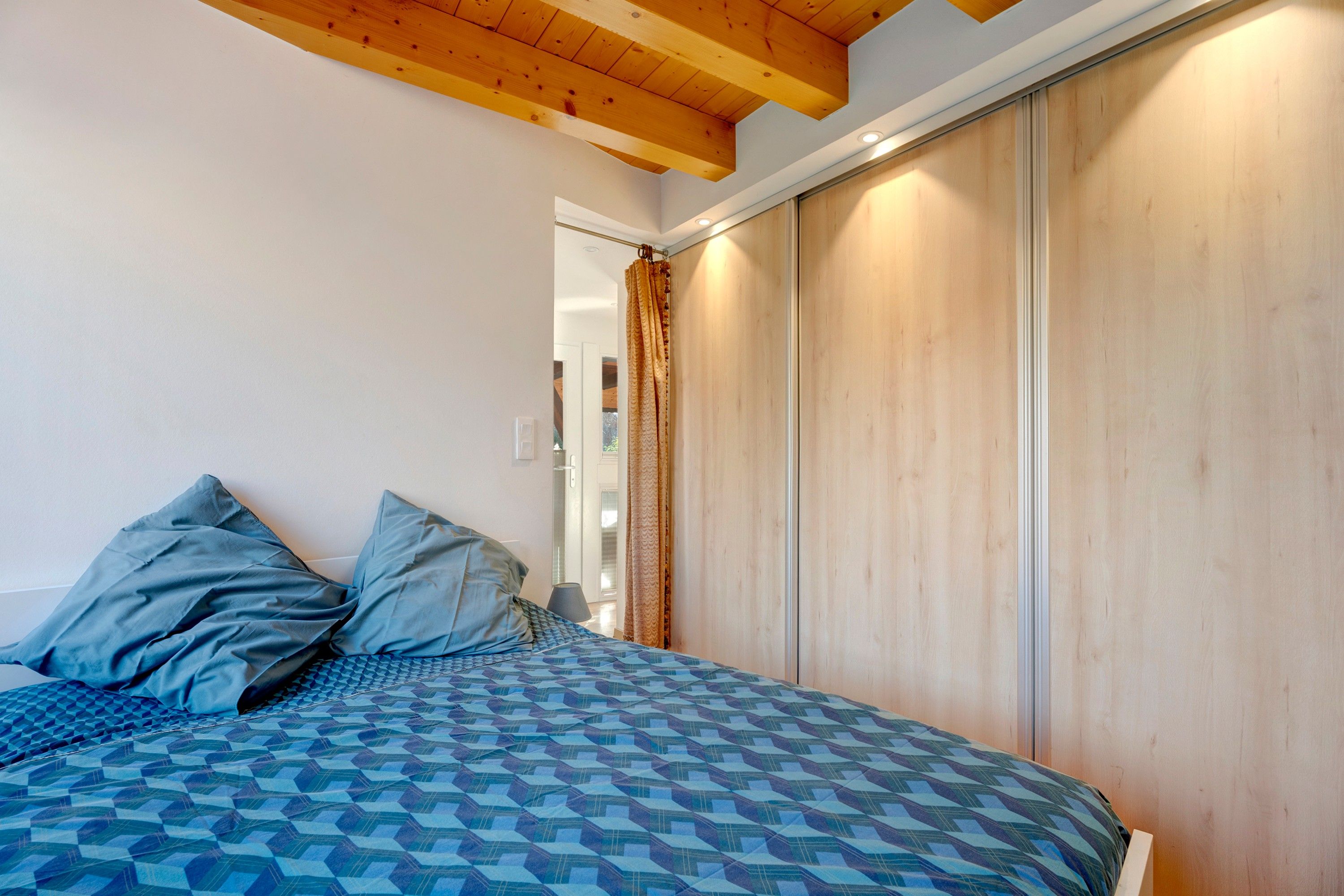 A bedroom with a bed, pillows, a wooden wardrobe, and a window with curtains.