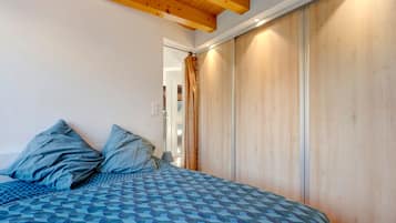 A bedroom with a bed, pillows, a wooden wardrobe, and a window with curtains.