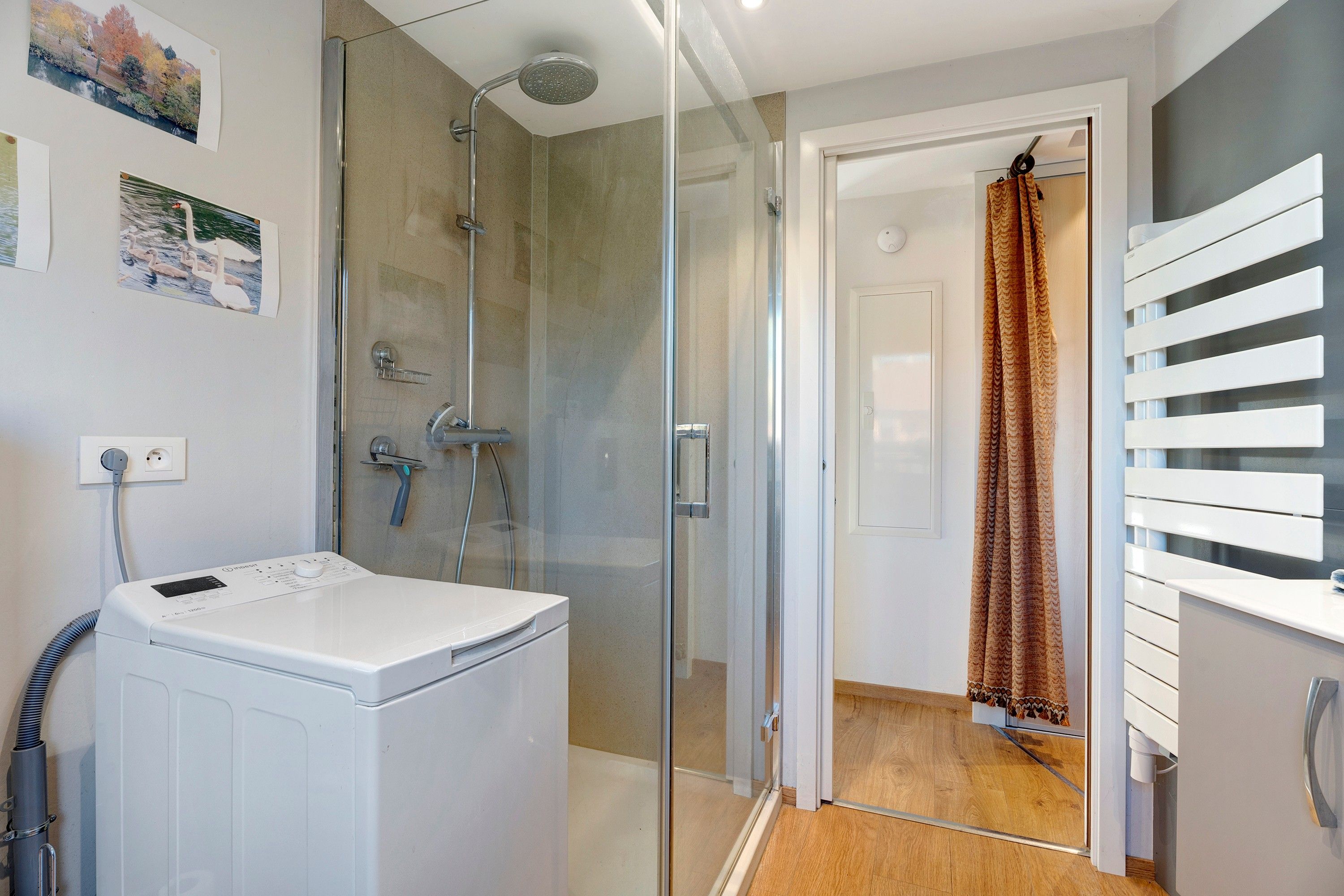 Un bagno moderno con cabina doccia in vetro, una lavatrice bianca e pavimento in legno.
