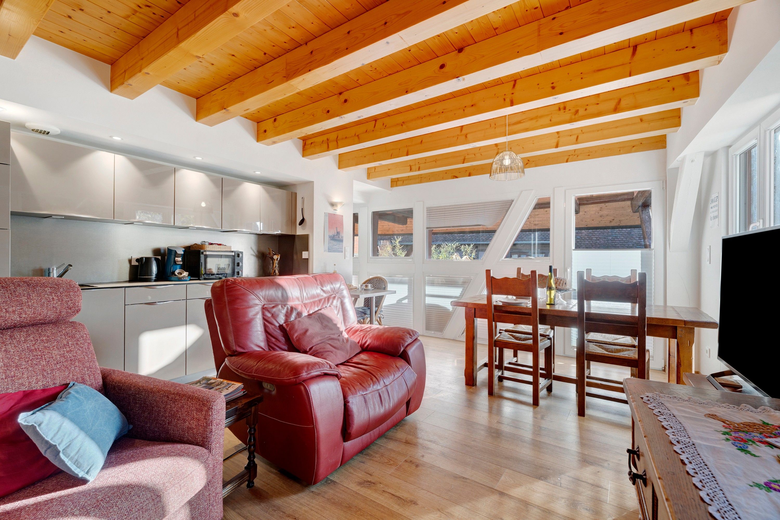 Un'ampia zona giorno con un divano in pelle rossa, un tavolo da pranzo in legno e una cucina sullo sfondo.
