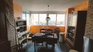 Un comedor con mesa y sillas, una lámpara colgante, una estantería y vistas al exterior a través de una ventana.