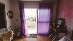 Una habitación con un ventanal grande, piso de madera, una mesita con un marco de foto y una silla.
