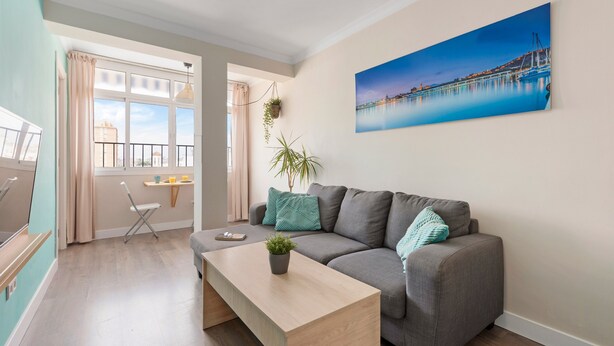 Un salon avec un canapé gris, une table basse en bois, une plante en pot et un tableau représentant un paysage côtier.