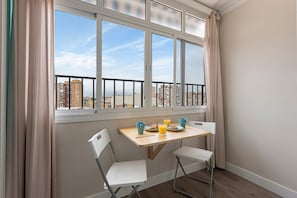 A dining area with a table and chairs, a window with a view of buildings, and curtains. - Apartment 'Málaga Beach, Costa del Sol' with Mountain Views, Wi-Fi & Air Conditioning (Málaga)
