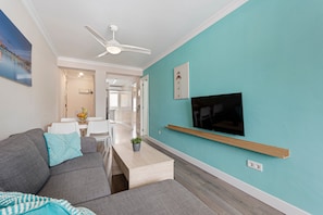 Ein modernes Wohnzimmer mit einer Couch, einem Couchtisch, einem an der Wand befestigten Fernseher und einem Deckenventilator.