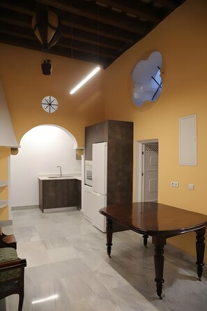 Un comedor con una gran mesa de madera, una cocina al fondo y un reloj de pared original.