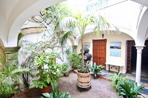 Un patio con arcos, plantas en macetas, una puerta de madera y una mesa con un cuadro.
