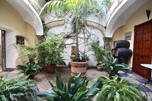 Une cour intérieure agrémentée de plantes en pot, d’une barrique en bois et d’un pilier en pierre.