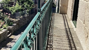 Un balcón con barandilla de metal verde, una pared de piedra y un tejado a la vista.