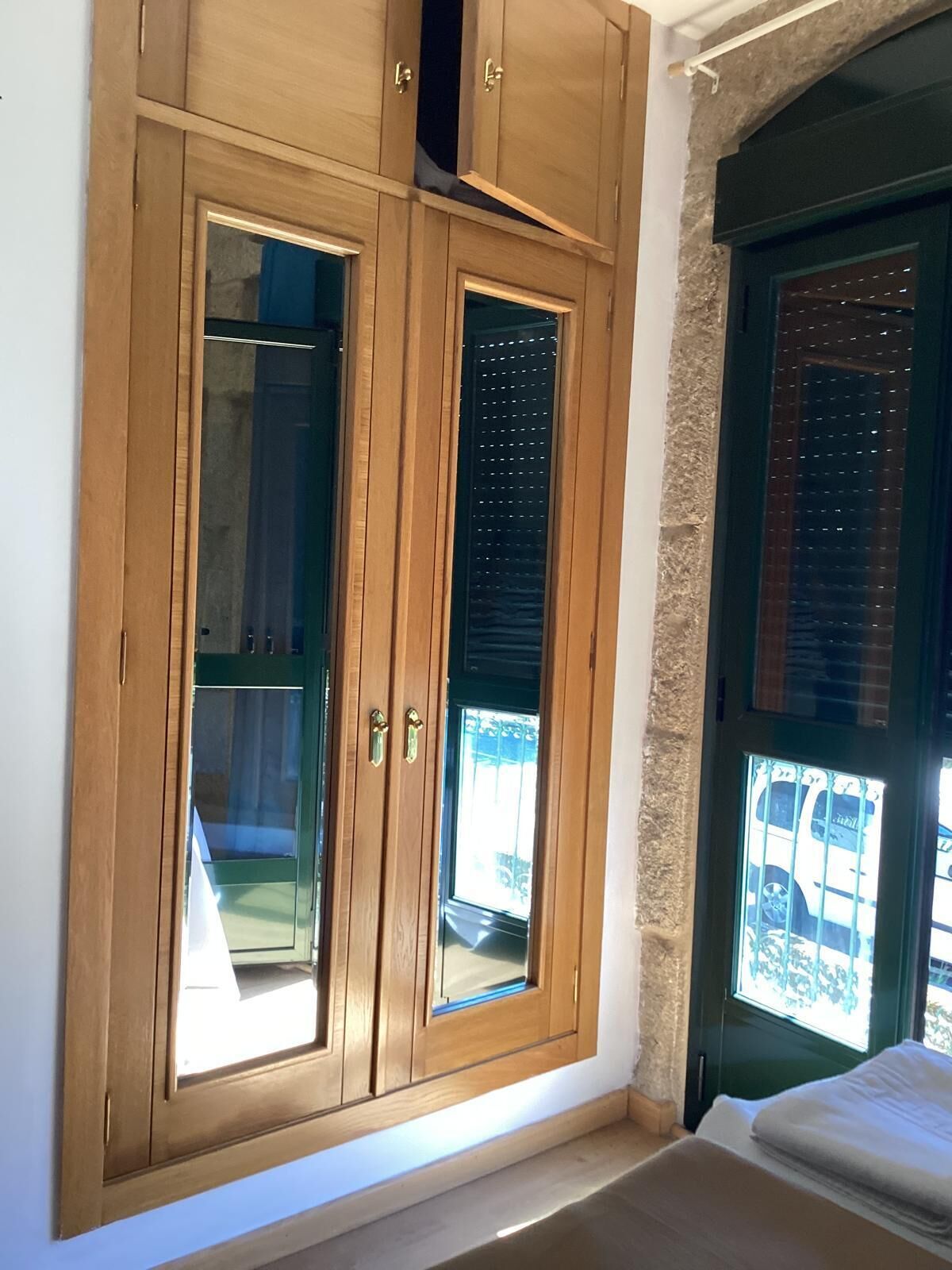 A room with a large wooden wardrobe, a bed, and a window with a view of parked cars.