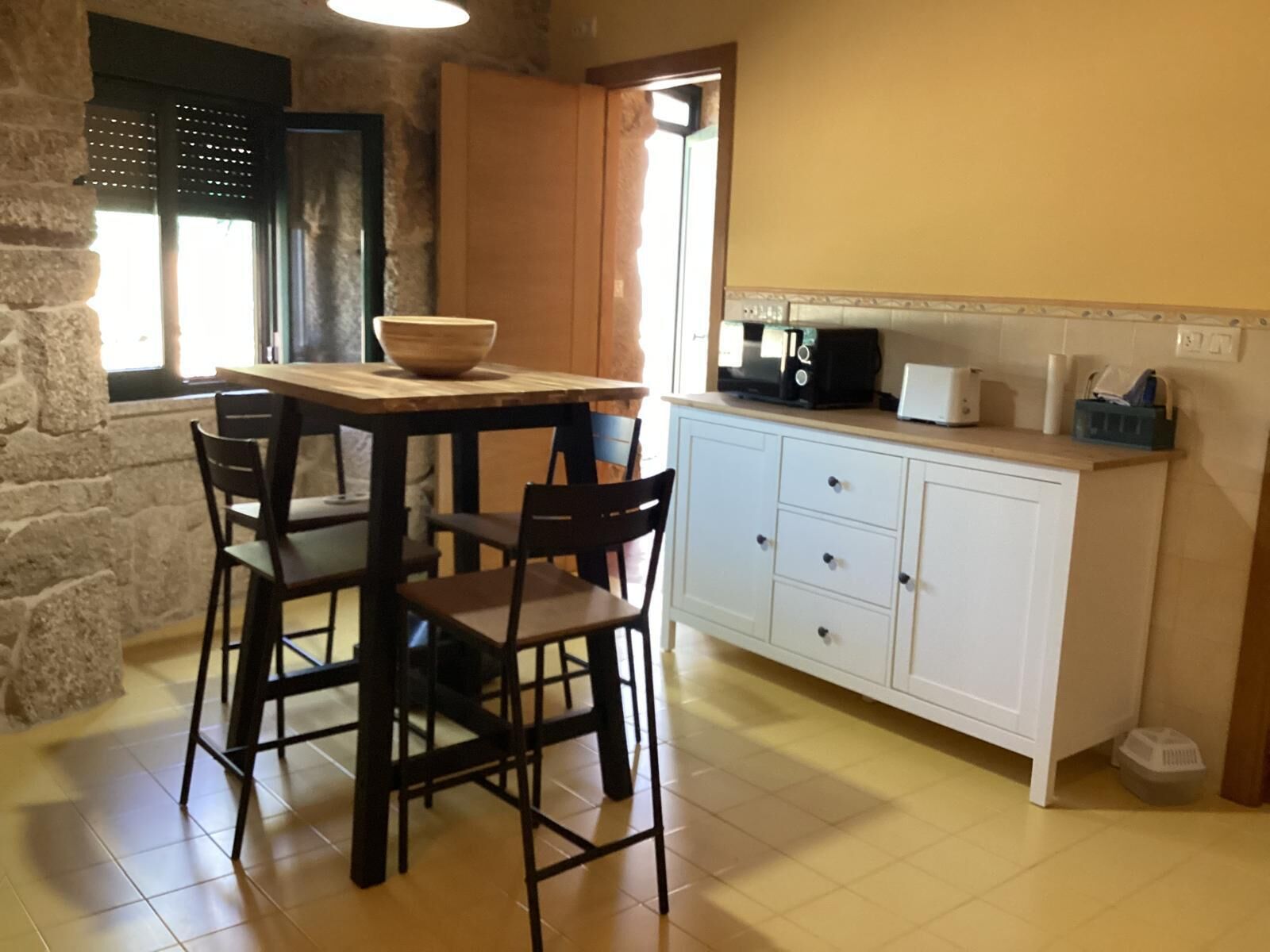 Une cuisine avec une table en bois, quatre chaises, un meuble blanc et un four à micro-ondes.