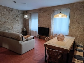 Una sala de estar con pared de piedra, un sofá, un televisor, una mesa de comedor con sillas e iluminación colgante.