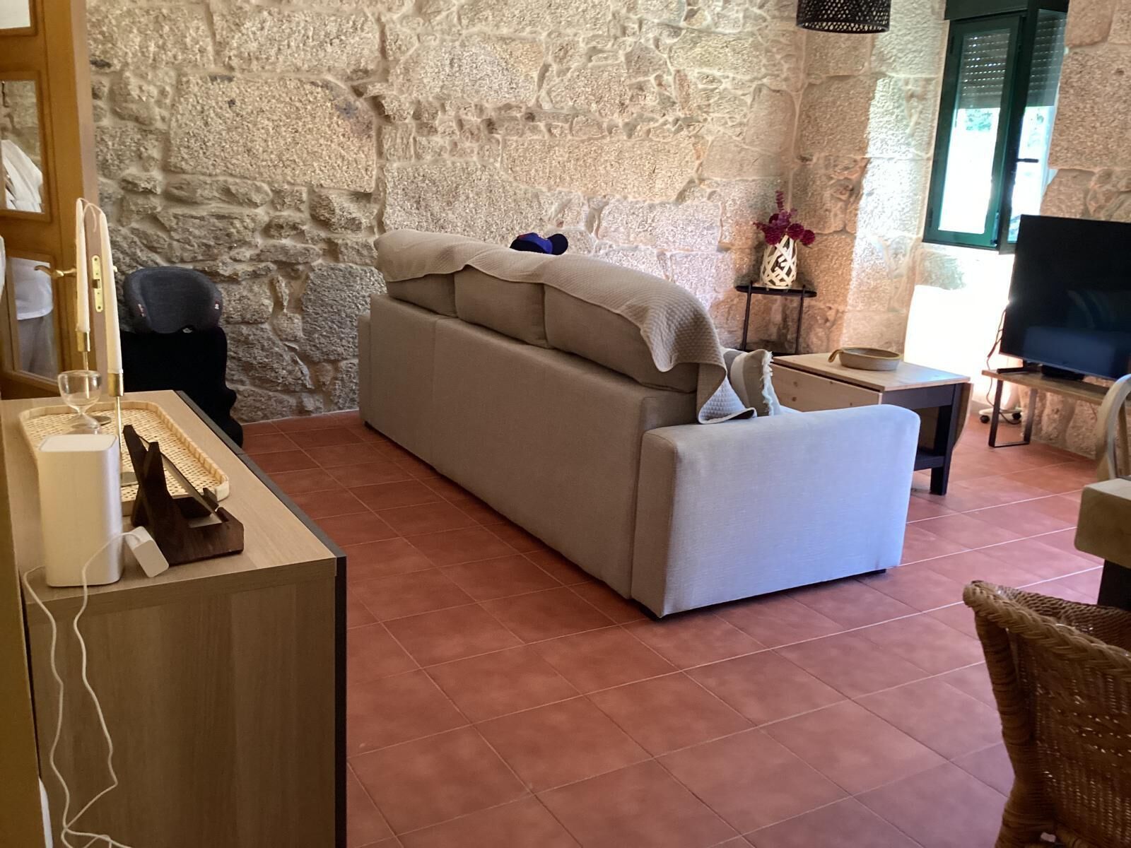 Una sala de estar con una pared de piedra, un sofá, un televisor y una pequeña mesa con un jarrón.