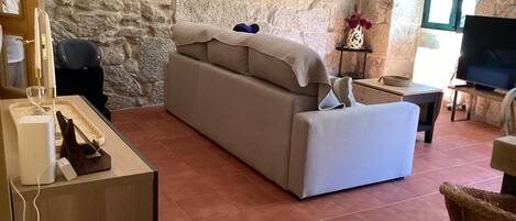 Una sala de estar con una pared de piedra, un sofá, un televisor y una pequeña mesa con un jarrón.