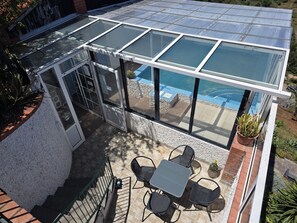 A glass-enclosed patio with a pool view, outdoor seating, and a potted plant. - Classic Panoramic View Ocean Apartment with Shared Pool, Garden and Wi-Fi (Gaula)