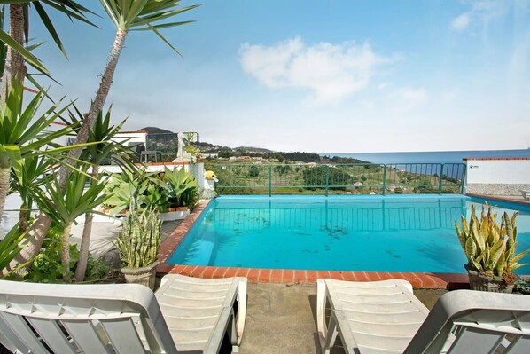 A swimming pool with a view of the sea, surrounded by plants and white lounge chairs. - Classic Panoramic View Ocean Apartment with Shared Pool, Garden and Wi-Fi (Gaula)