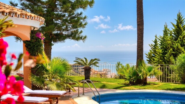 Una piscina con vista al mar, rodeada de palmeras y una pérgola con flores.