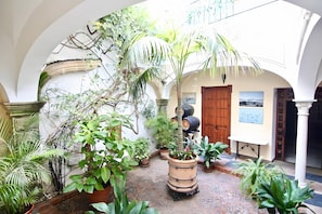 A courtyard with arches, potted plants, a wooden door, and a table with a picture. - Apartment 'Capitán De Navio' with Balcony, Wi-Fi and Air Conditioning (El Puerto de Santa María)