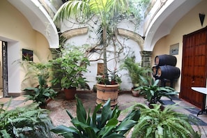 An indoor courtyard with potted plants, a palm tree, and a barrel. - Apartment 'Capitán De Navio' with Balcony, Wi-Fi and Air Conditioning (El Puerto de Santa María)